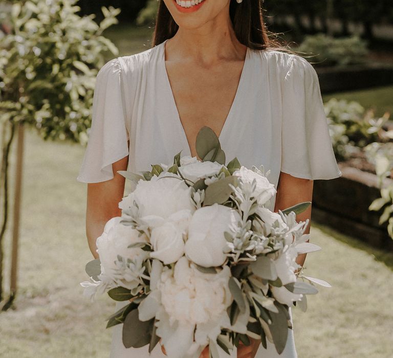 Bride in a white satin Ghost wedding dress and chunky pearl headband with a white flower wedding bouquet 