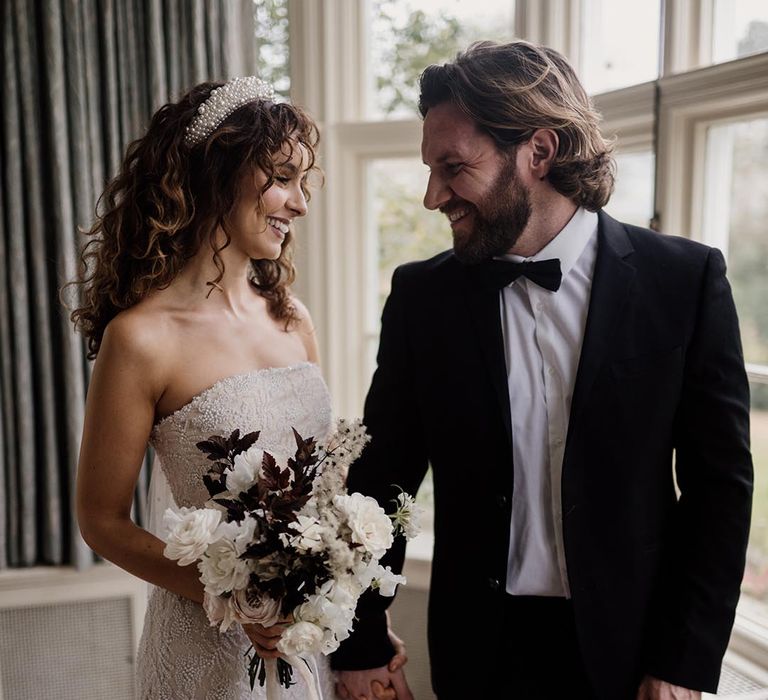 Bride in sleeveless lace detail wedding dress with pearl headband and minimalist black and white bouquet and groom in black tux 