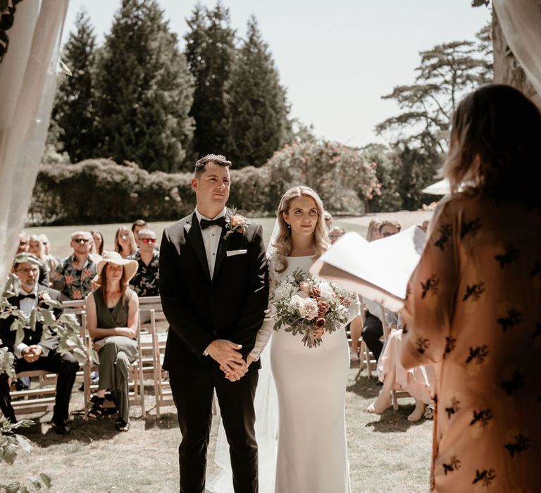 Bride and groom stand at the altar for the outdoor wedding ceremony at Pennard House with pretty wedding drapes 