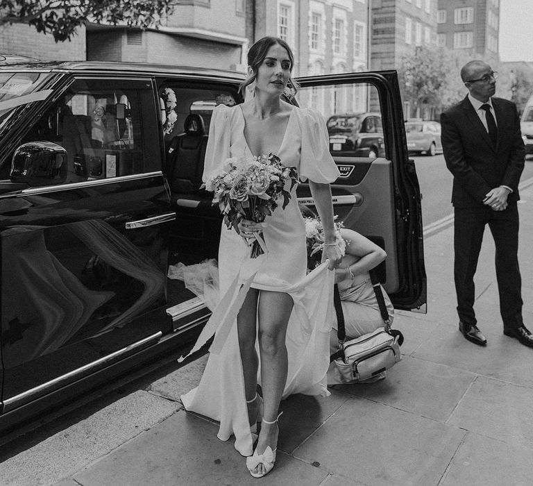 Bride getting out of a taxi wearing modern puff sleeve wedding dress with v neck cut and front slit