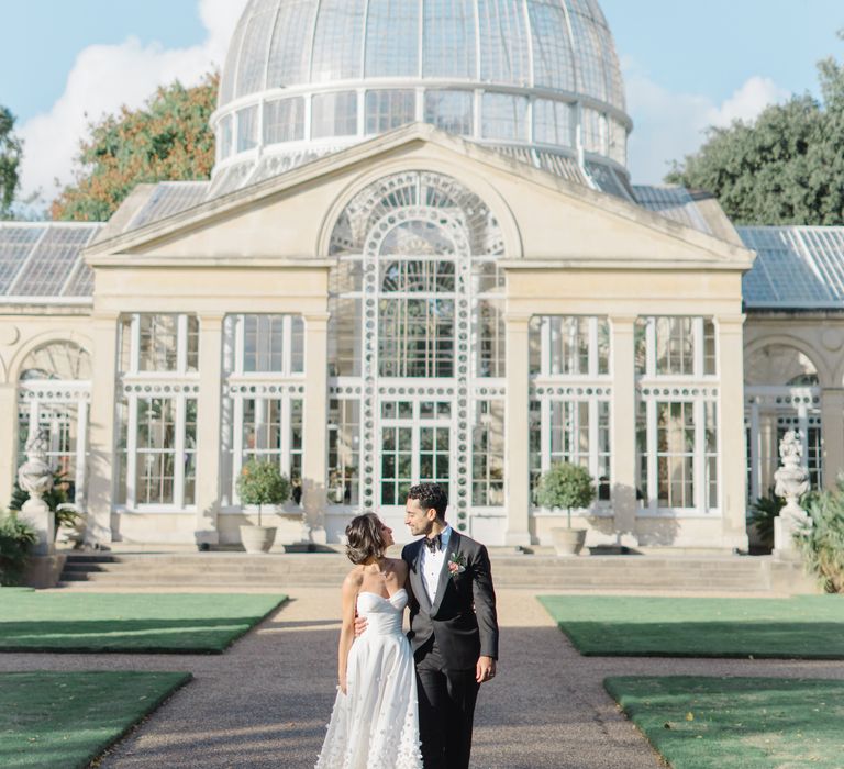 Bride & groom stand in front of Syon Park Conservatory 