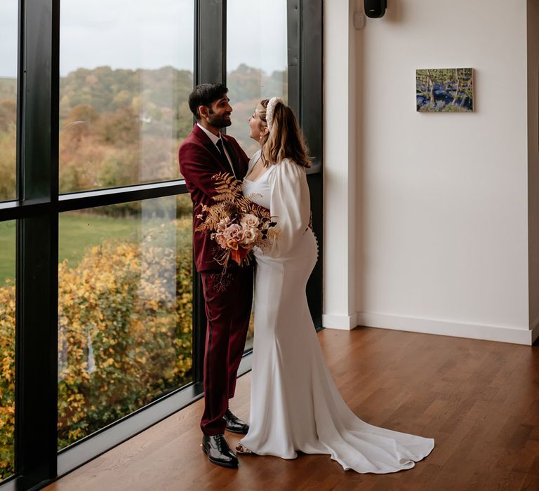 Groom in burgundy suit and black lapels with bride in square neckline long sleeve wedding dress with pearl headband 