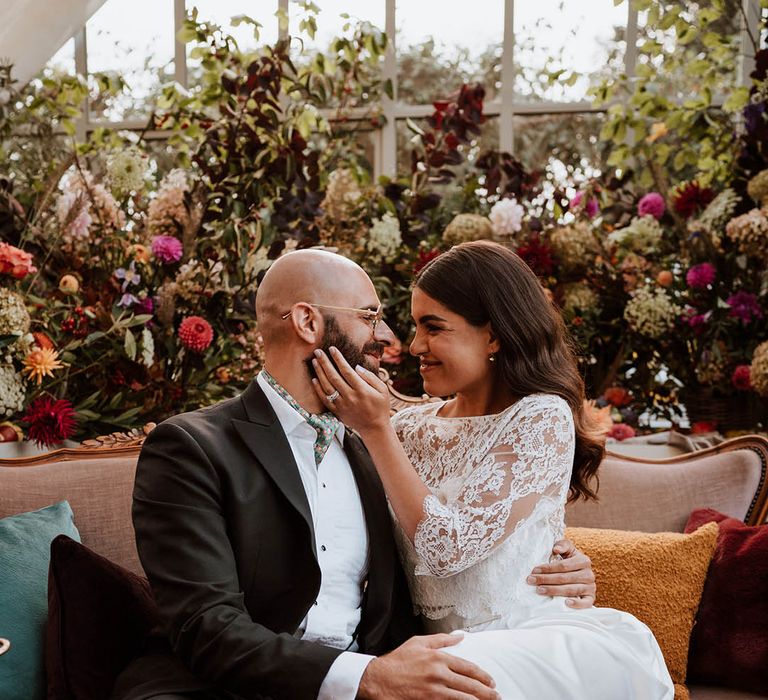 Bride in three quarter length sleeve wedding dress with lace detailing and full satin skirt and bottle green satin wedding shoes and groom in classic black tuxedo with hand-painted silk cravat and handkerchief embracing each other 