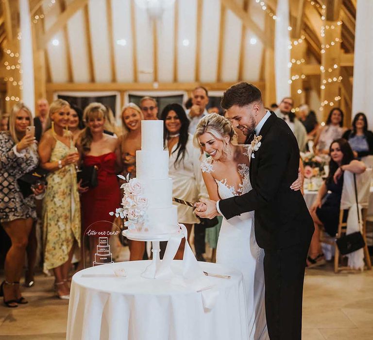 Bride and groom cutting four tiered buttercream wedding cake with blush pink rose decorations and blush pink lace ribbon 