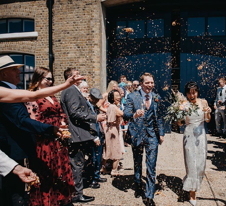 Bride in silver wedding dress walks through colourful confetti exit with her groom at Trinity Buoy Wharf 