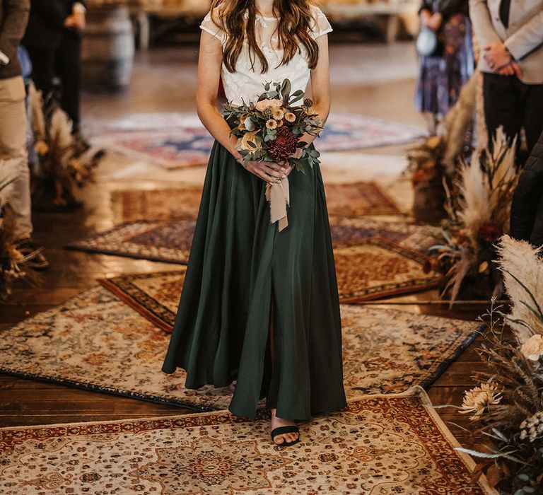 Bridesmaid in green silk skirt and white top walks down the aisle 