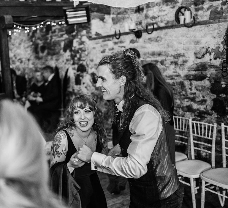 Bride in v-neck black wedding dress and groom in alternative groom suit dancing to live wedding band at boho themed wedding 