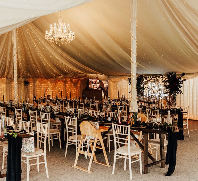 Marquee wedding at Parley Manor with black wedding cake and decor including fairy lighting and chandelier as well as a neon sign on a glitter wall 