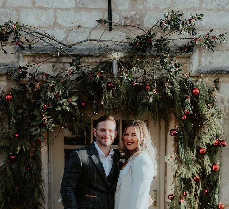 Floral arch entrance decoration made up of festive Christmas foliage and decorations including red baubles and fairy lights 