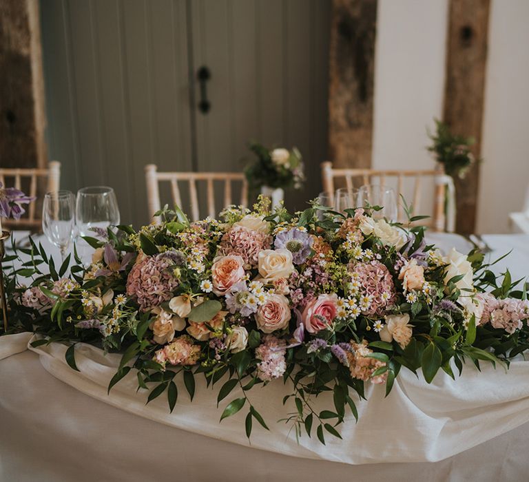 Pastel wedding flowers with roses and hydrangeas decorating the top table 