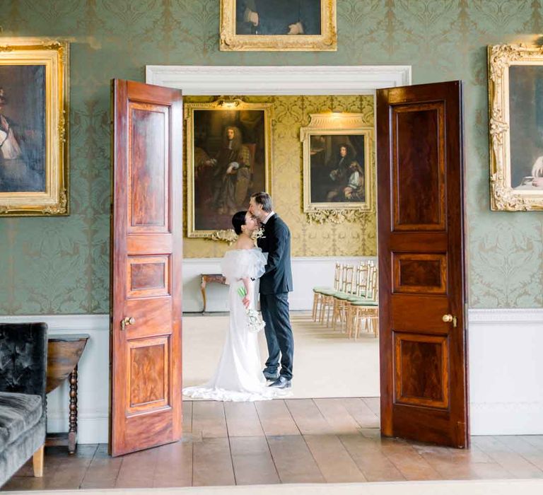 Bride and groom sharing embrace at St Giles House with dramatic gold framed portraits and forest green wallpaper 