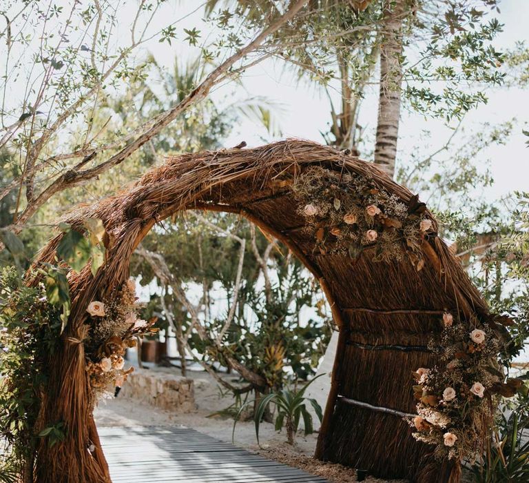 Large bamboo wedding arch on beach at destination wedding in Mexico with dried garden flower and foliage flower arrangements 