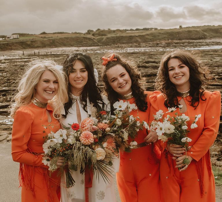 Bride in sparkly jumpsuit and bridesmaids in bright orange jumpsuits by Bowen Dryden 