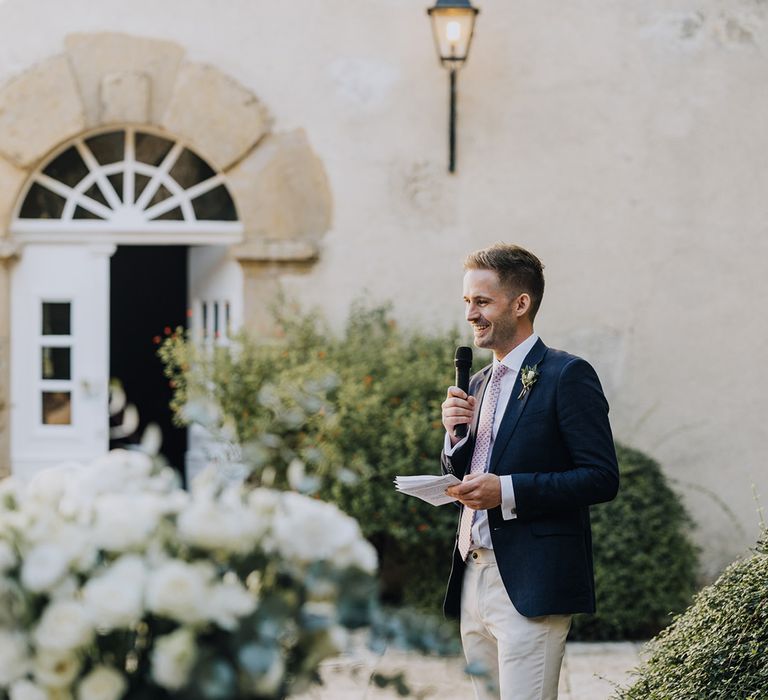 Groomsman in stone chinos and a navy blazer giving a wedding speech during the al-fresco reception 