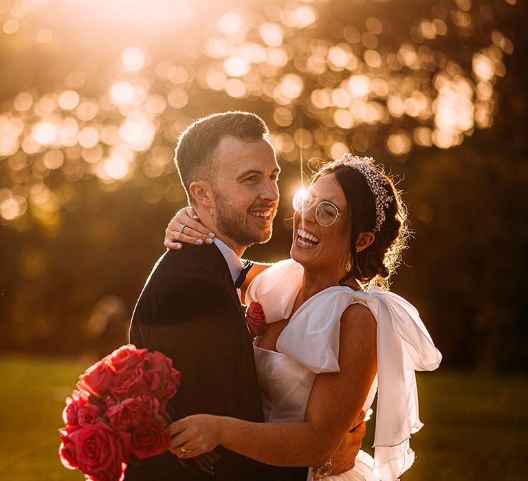 Groom embraces the bride wearing a stunning gold crown and glasses in ruffle bow wedding dress 