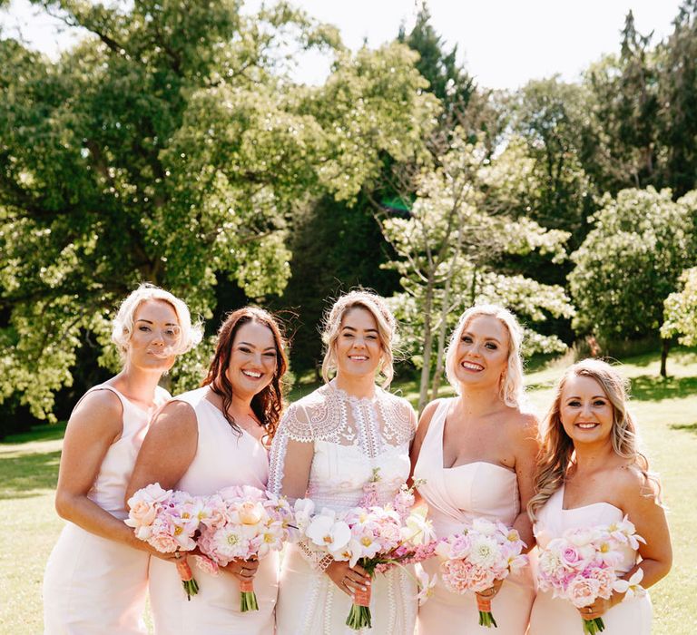 Bridesmaids in pink one shoulder bridesmaid dresses with bride in long sleeve lace wedding dress holding pink bouquets 