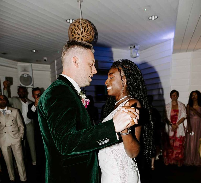 Bride in v neck sleeveless lace Pronovias wedding dress doing wedding first dance with groom in bottle green velvet grooms blazer, colourful tropical boutonniere and black suit trousers 