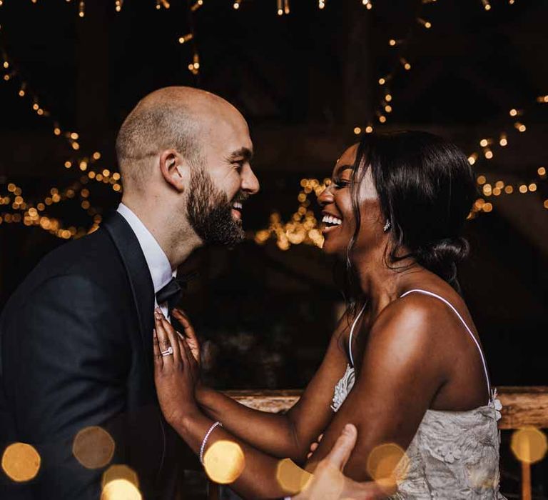 Bride and groom embracing and laughing surrounded by wedding fairy lights and festoon chandeliers in Lains Barn reception room