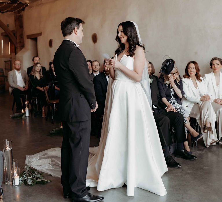 Bride and grrom stand at the alter and read personalised vows to each other with fairy lights above them at Upton Barn wedding venue