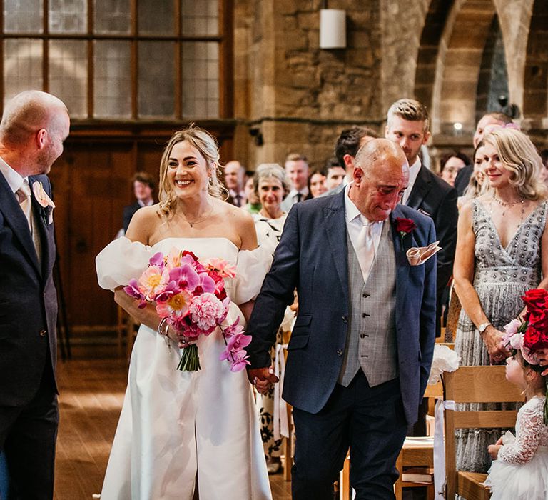 Father of the bride holds back his tears as he walks the bride down the aisle to meet the groom 