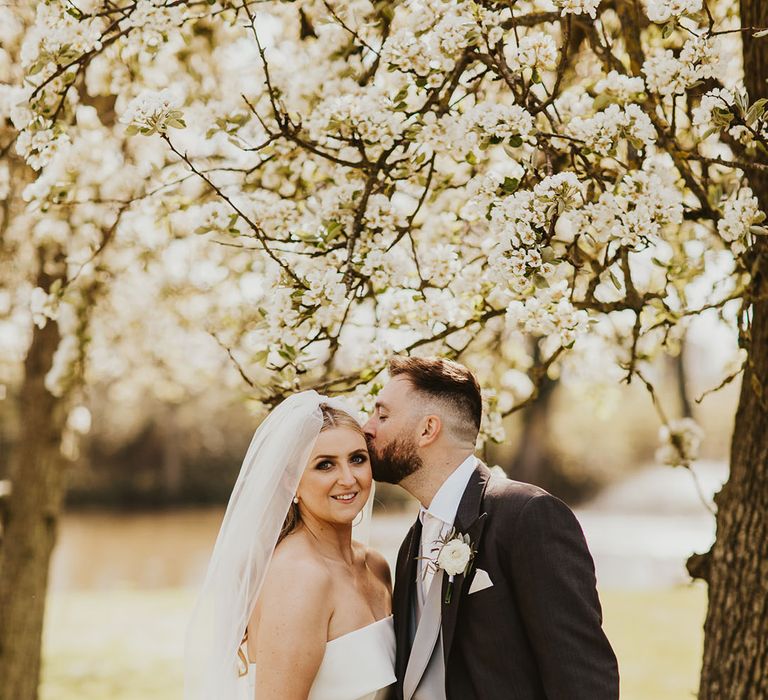 Bride in strapless Eva Lendel wedding dress kissing the groom in black and grey wedding suit at Villiers Barn wedding venue 