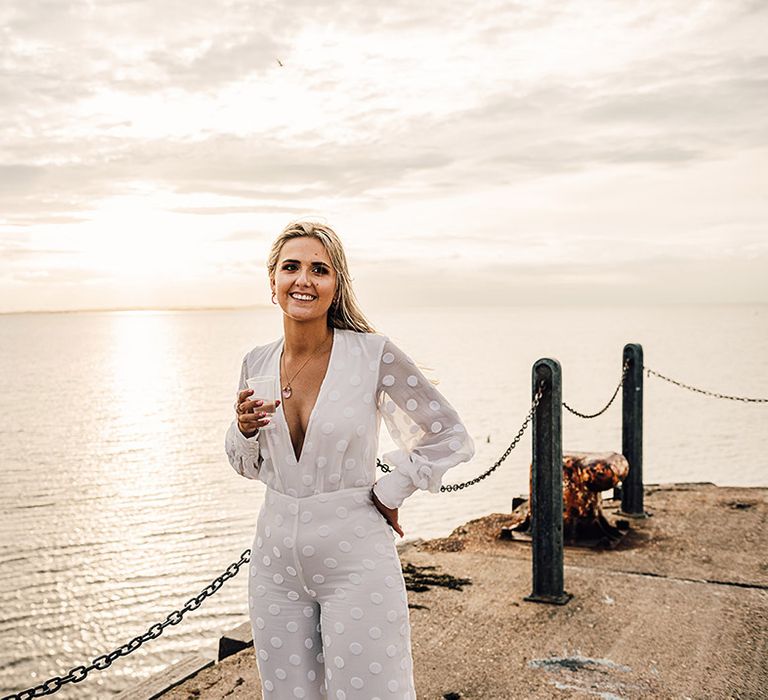 bride drinking champagne by the beach in a long sleeve and wide leg Nikeen Asar jumpsuit at coastal wedding 