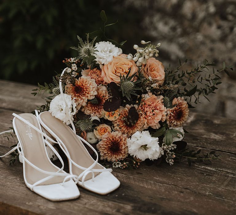 Orange and white bridal bouquet next to white wedding heels for bride