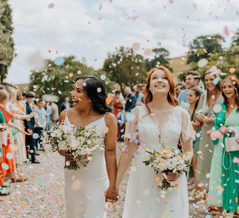 Pastel colourful confetti exit for the two brides after their outdoor ceremony at Lyde Court 