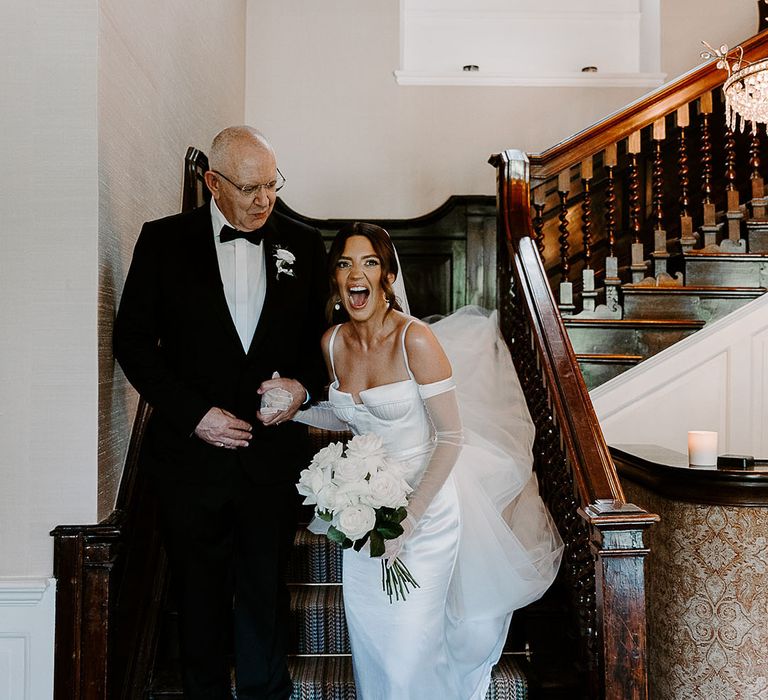 Father of the bride in black tuxedo walking with bride in satin wedding dress 