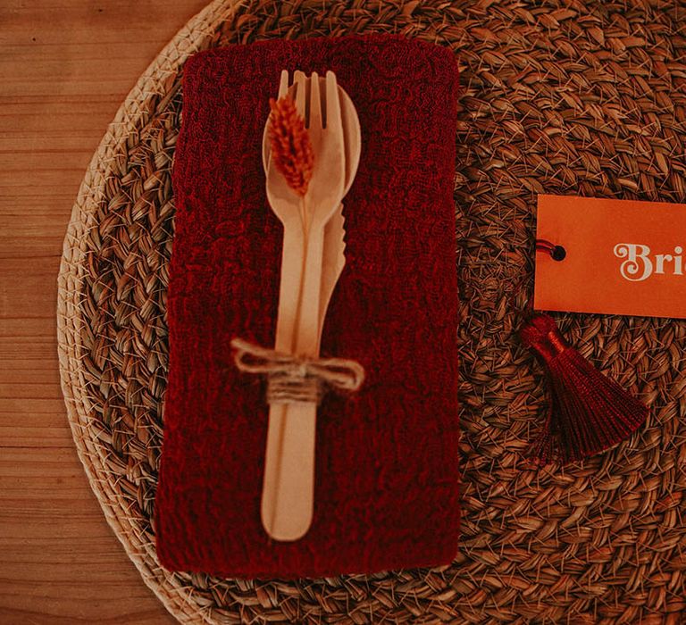 Autumnal orange wedding place setting with wooden cutlery, orange wedding place name and red napkin on wicker placemat 