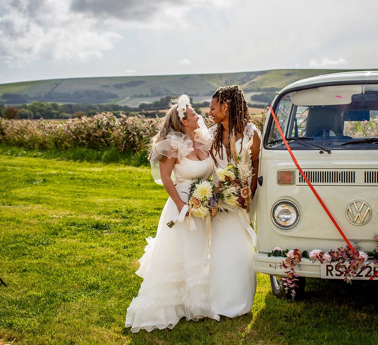 Same sex lesbian wedding with two brides kissing next to their campervan wedding transport 