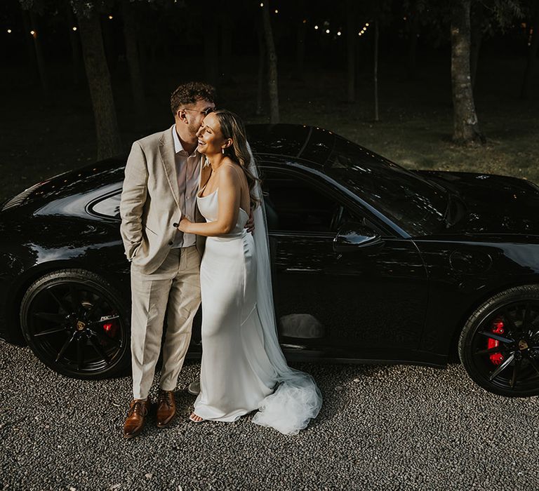 Bride and groom share a kiss next to their sports car wedding transport 