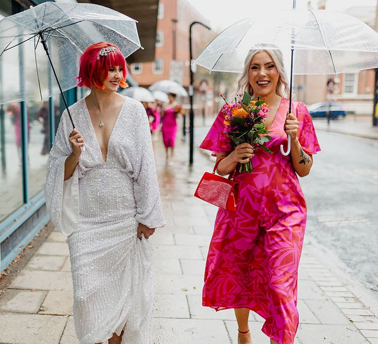 Bridesmaid in pink and orange bridesmaid dress with the bride in a sequin wedding dress on rainy wedding day 