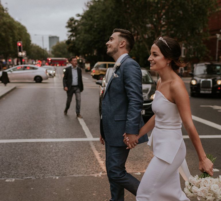 Stylish bride in strapless Roland Mouret wedding dress and groom in blue suit walking through London