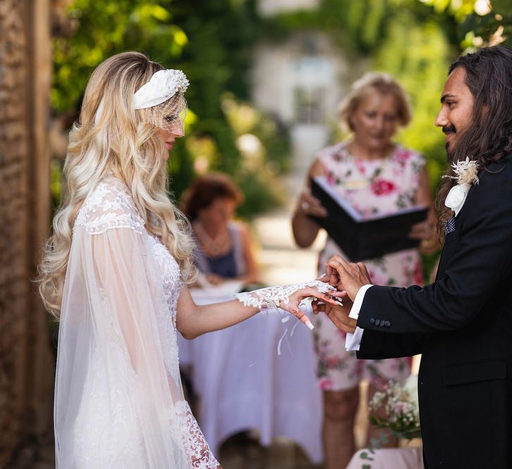 Groom in black suit putting on his brides wedding ring 