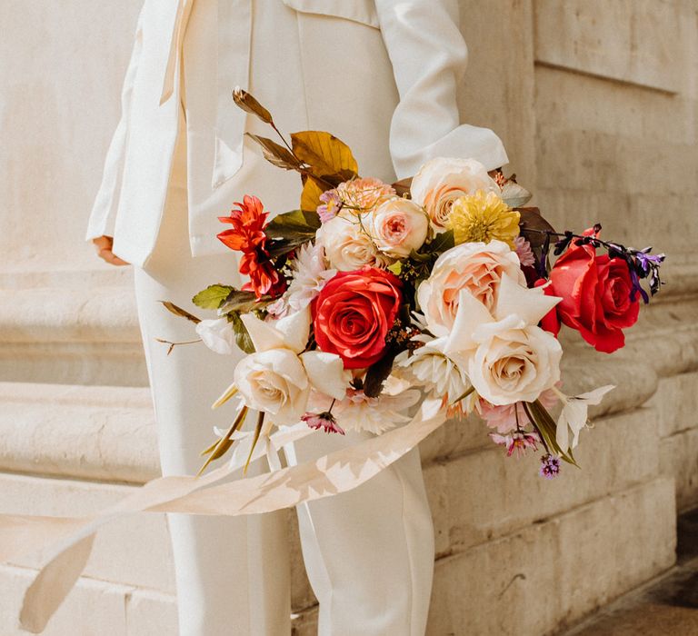 Bride in a trouser suit holding a brightly coloured wedding bouquet 