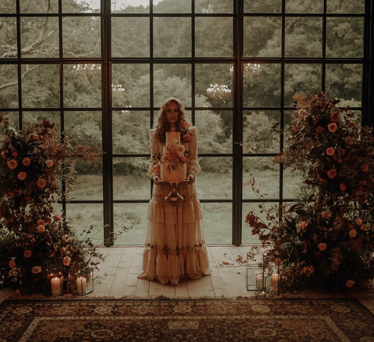 Bride in a vintage wedding dress holding a wedding cake 