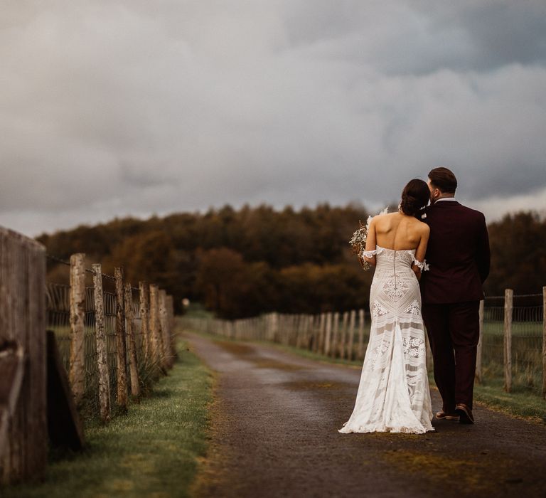 Bride in sleveless boho wedding dress walking arm-in-arm with groom in the Lake District