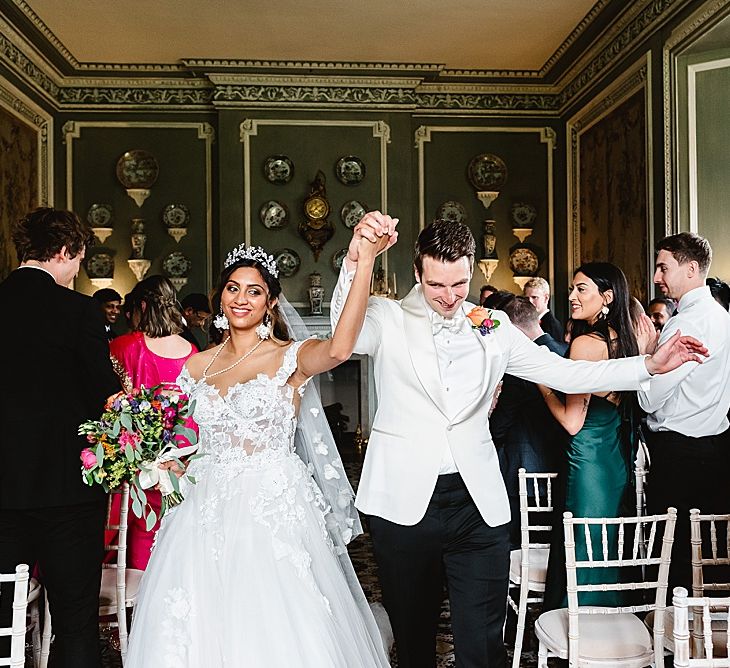 Bride in a Galia Lahav wedding dress and groom in a white dinner jacket descending down the aisle as husband and wife