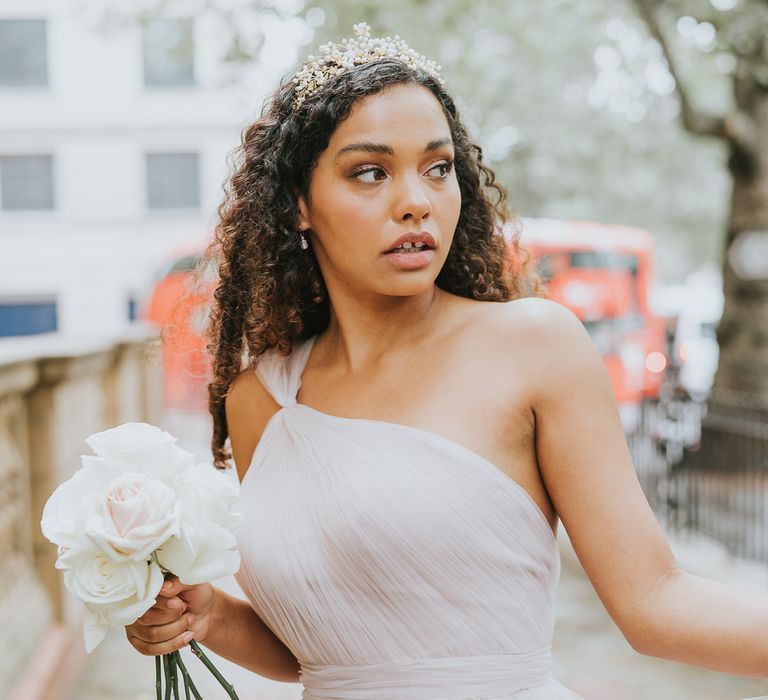 Bridesmaid with naturally curly hair wearing a one shoulder chiffon bridesmaid dress and holding a white rose bouquet 