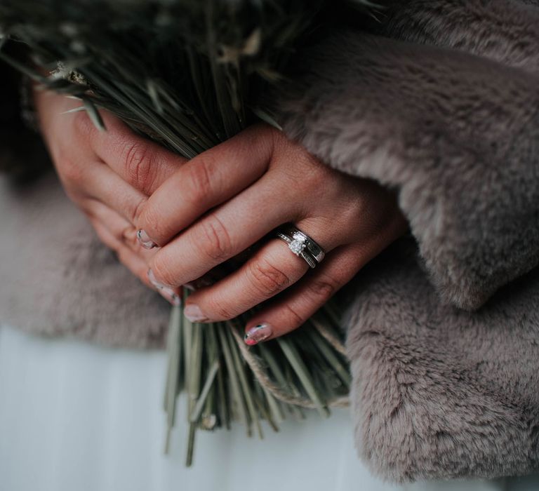 Close up of brides wedding ring with colourful nails and dried flower bouquet 