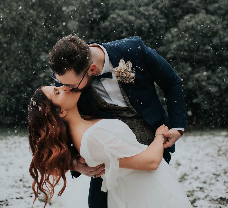 Bride with glam waves and groom in navy suit kiss in the grounds at Cannon Hall after snowy wedding