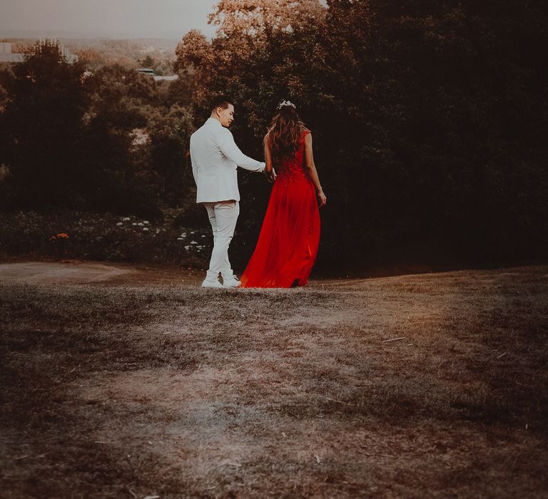 Groom walks along with bride wearing red reception gown