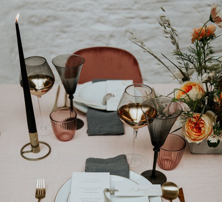 A luxe contemporary table setting with blush pink and slate grey linens, velvet chairs and dark coloured glassware