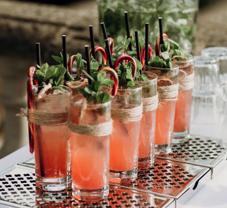 Coral cocktails in long glasses garnished with mint leaves and striped candy canes by the Mixology Brothers at Euridge Manor wedding