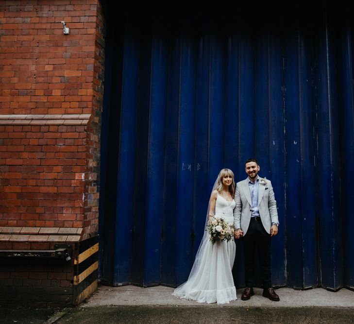 Bride and groom pose against blue industrial steel door