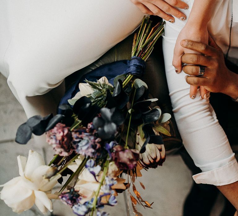 Bride and groom holding hands with the purple and white wedding bouquet resting close by 