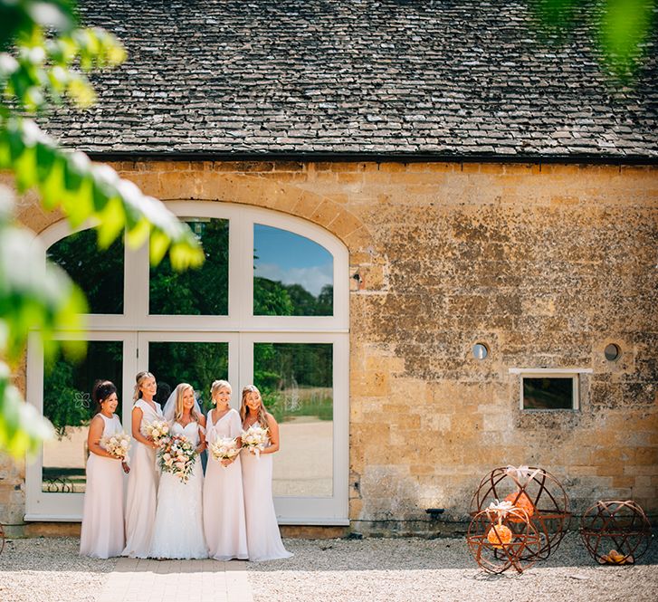 Country wedding with bride stood outside barn with her bridesmaids 