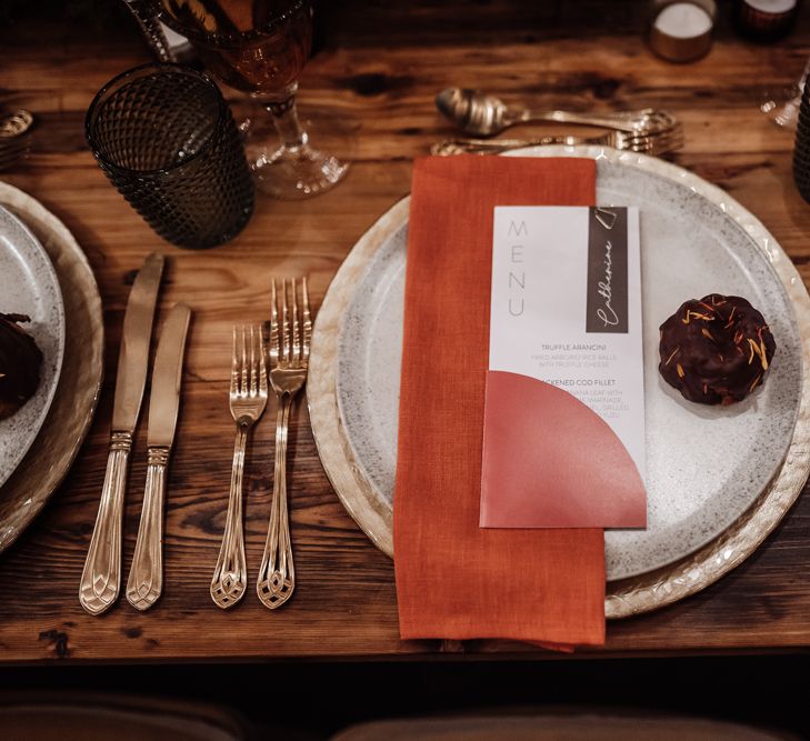 Place setting with dappled tableware, orange napkin and contemporary menu sign 