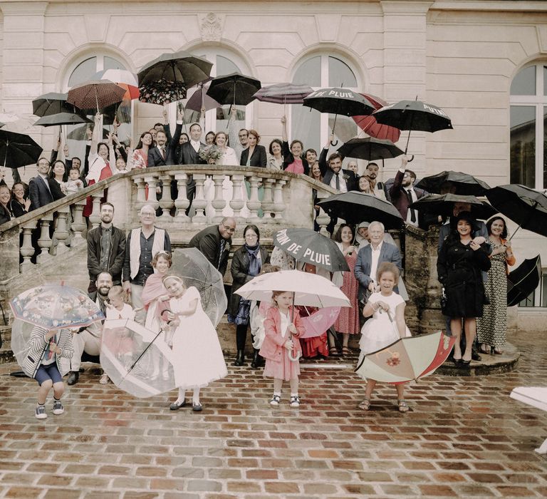 The bride and groom and their 60 guests all smiling for the camera and holding up umbrellas